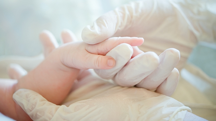 Gloved hand holding a newborn baby's hand. Image from the American Association for Respiratory Care.
